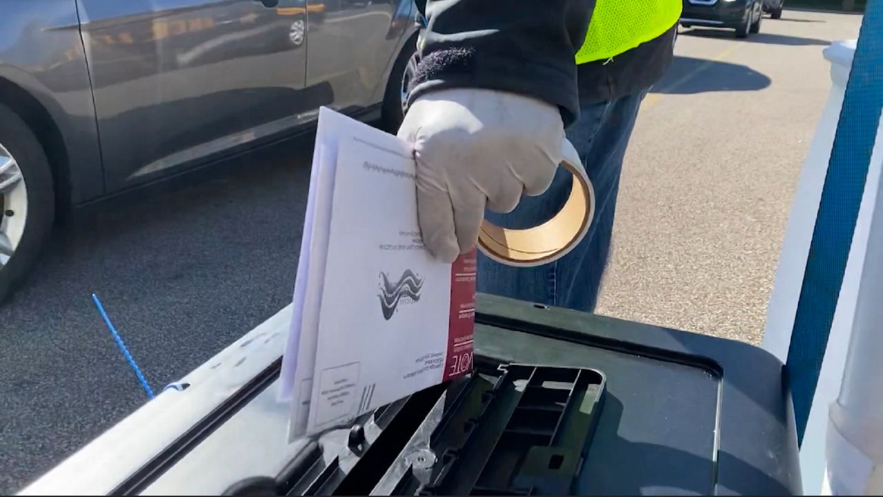 Poll worker in gloves drops voting ballots into a main-in box (Spectrum News/File)