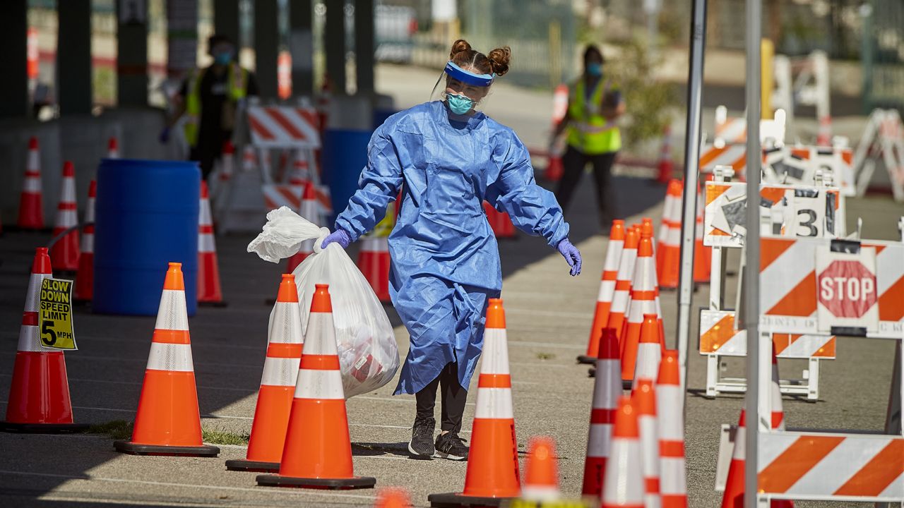 A medical worker wearing protective gear collects a bag with kits that motorists had used to swab themselves at a COVID-19 drive-up testing site at East Los Angeles College on Thursday, April 30, 2020, in Monterey Park, Calif. (AP Photo/Damian Dovarganes)