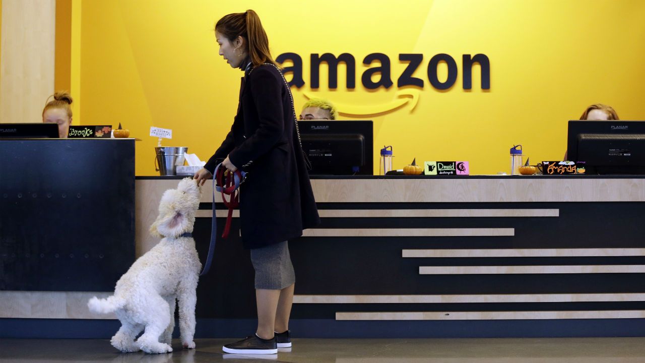 In this Wednesday, Oct. 11, 2017, photo, an Amazon employee gives her dog a biscuit as the pair head into a company building, where dogs are welcome, in Seattle. Whichever city lands Amazon’s second headquarters, some people in Seattle, it’s original hometown, say there are downsides to having the tech giant in the neighborhood. (AP Photo/Elaine Thompson)
