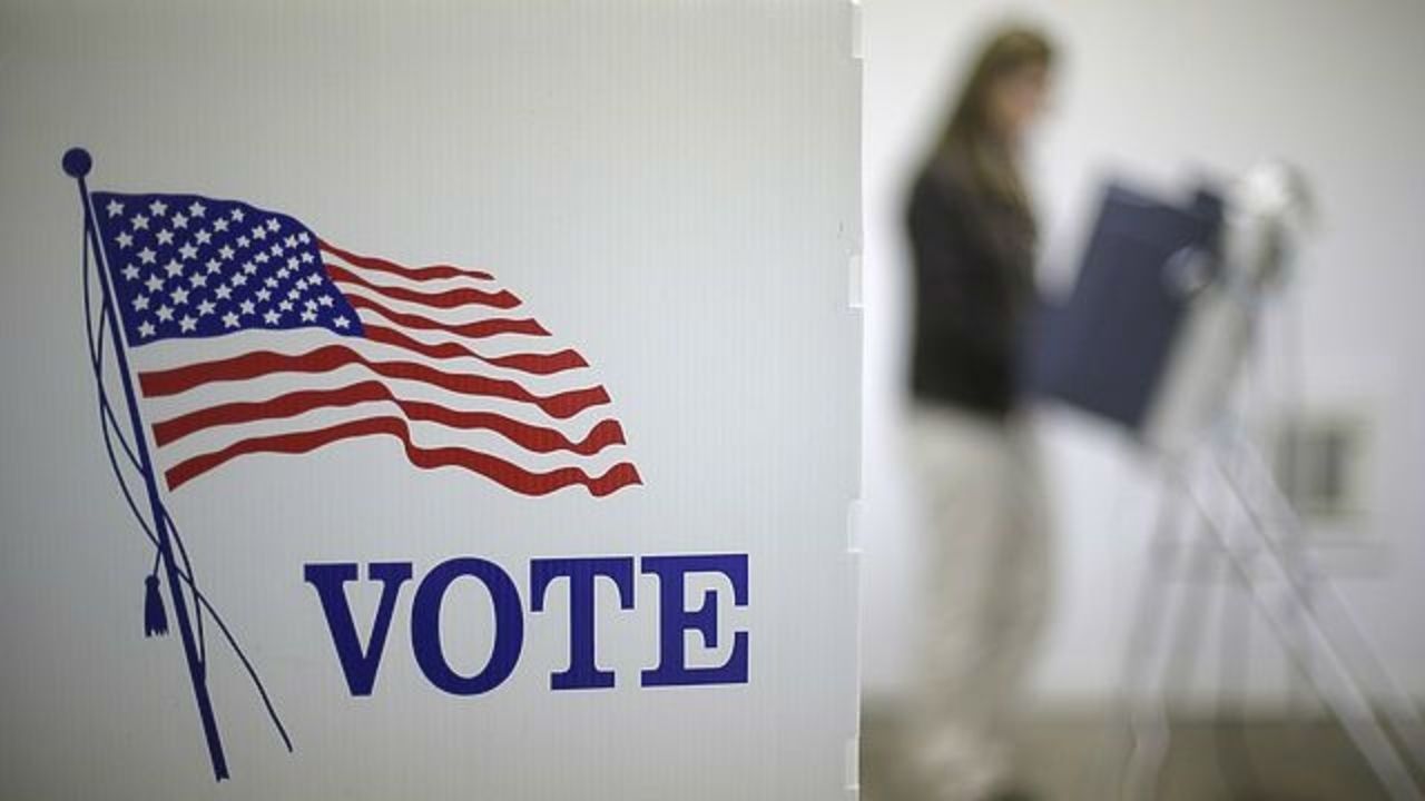 An image of an American flag printed on a white poster, with the message "Vote." A person stands in the background.