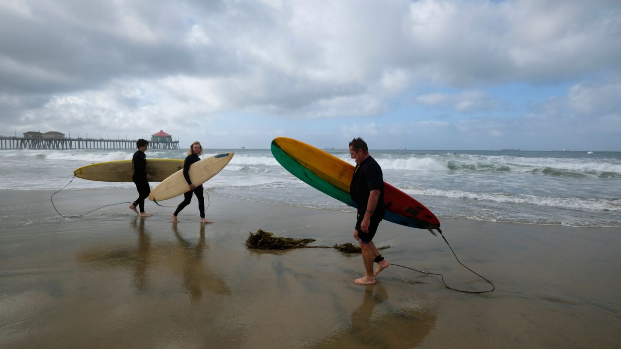 People get ready to surf on a beach in Huntington Beach, Calif., Monday, Oct. 11, 2021. (AP Photo/Ringo H.W. Chiu)