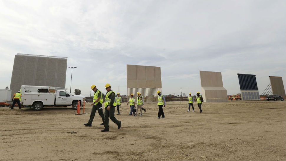 People pass border wall prototypes as they stand near the border with Tijuana, Mexico, Thursday, Oct. 19, 2017, in San Diego. Companies are nearing an Oct. 26 deadline to finish building eight prototypes of President Donald Trump's proposed border wall with Mexico.  GREGORY BULL / AP
