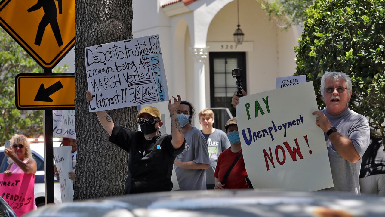 In this file photo from May 20, 2020, protesters wave signs at Florida Gov. Ron DeSantis as he and Vice President Mike Pence visit Orlando's Westminster Baldwin Park, a senior living facility. That same day, Pence and DeSantis participated in a roundtable discussion with Florida hospitality and tourism industry leaders over the coronavirus pandemic. (Chris O'Meara/AP)