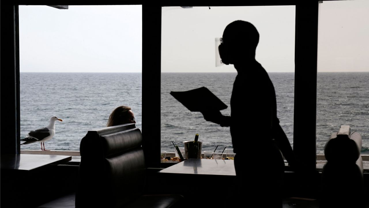 A waiter walks through an empty dining room as diners eat outside in front of beach views at Gladstone's restaurant Sunday, March 14, 2021, in the Pacific Palisades section of Los Angeles. (AP Photo/Mark J. Terrill)