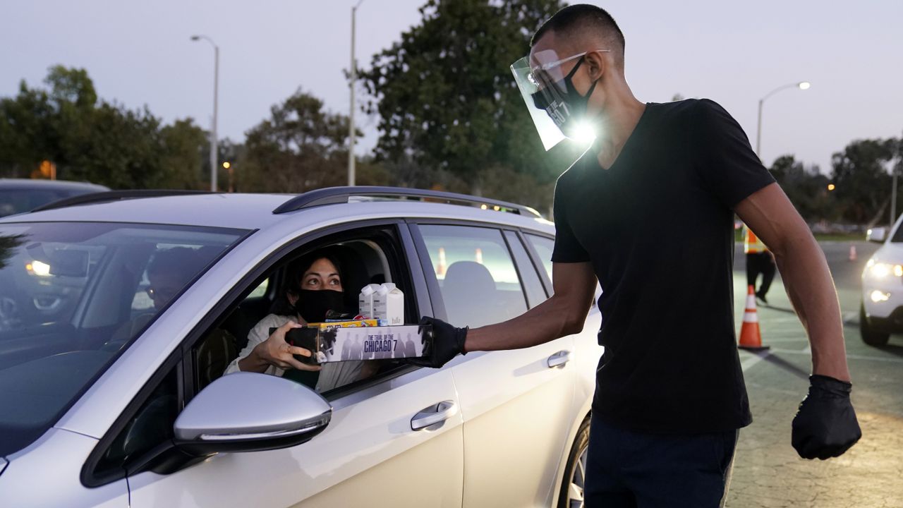 Riley Nunes, right, delivers concessions to audience member Morgan Rojas at the drive-in premiere of the Netflix film "The Trial of the Chicago 7," Tuesday, Oct. 13, 2020, at the Rose Bowl in Pasadena, Calif. (AP Photo/Chris Pizzello)