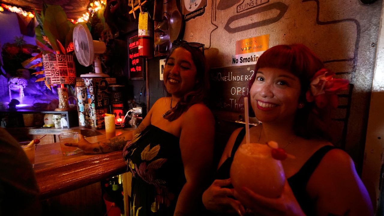 Patrons Verona Leyva, left, and Michelle Perez enjoy cold tropical cocktails in the tiny interior of the Tiki-Ti bar as it reopens on Sunset Boulevard in Los Angeles, Wednesday, July 7, 2021. (AP Photo/Damian Dovarganes)