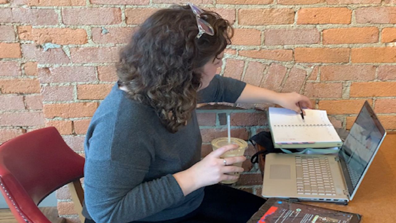 Woman reading a book, holding a drink and working on a computer