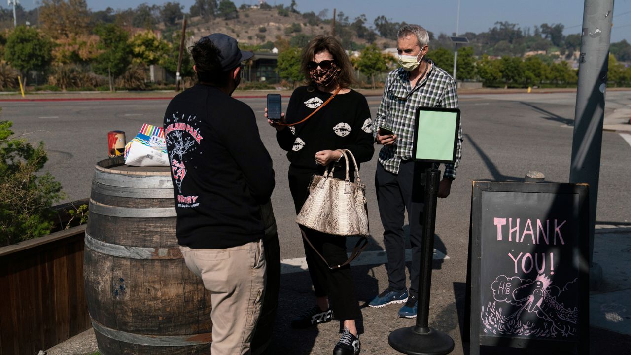 Marta McKay, center, and her husband, Bob, show a restaurant worker their proof of COVID-19 vaccination as they enter Highland Park Brewery Monday, Nov. 8, 2021, in Los Angeles.