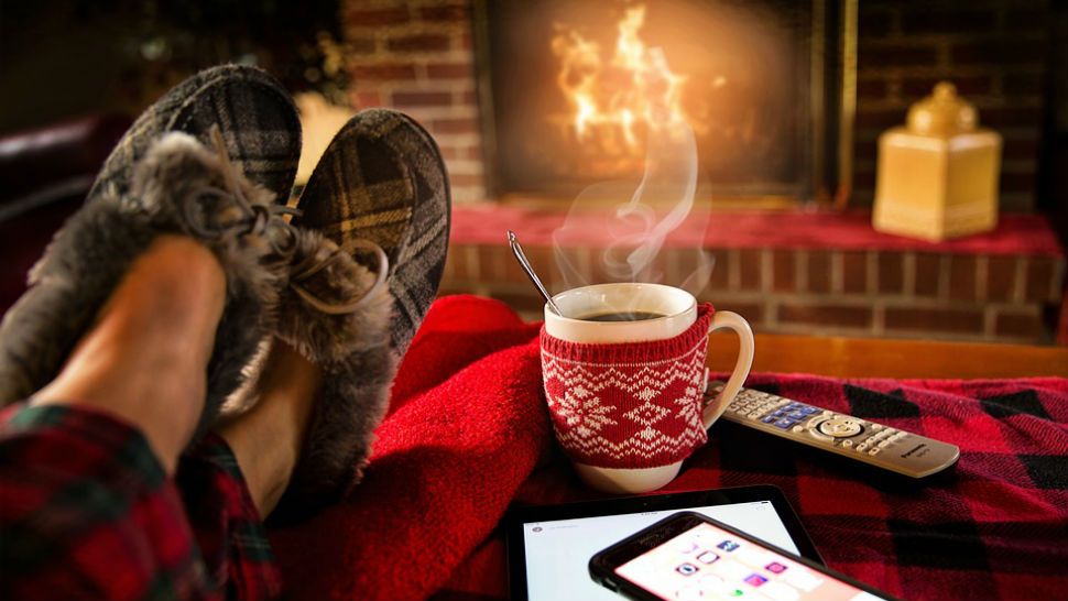 FILE photo of a person lounging in slippers sipping tea by a fireplace. (Pixabay)