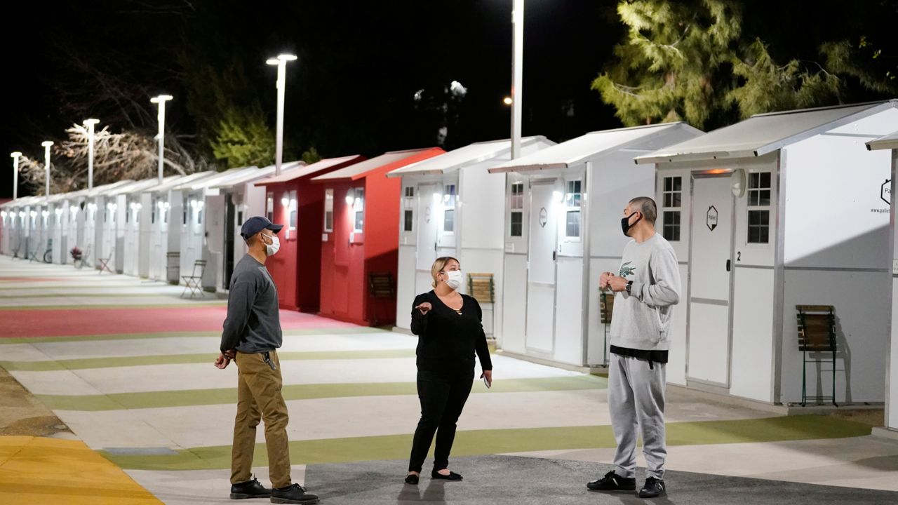 Workers talk to a resident, at right, in front a row of tiny homes for the homeless, Thursday, Feb. 25, 2021, in the North Hollywood section of Los Angeles. (AP Photo/Marcio Jose Sanchez)