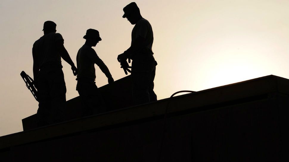 A silhouette of three men working on a roof.