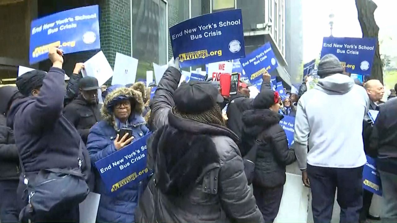 A crowd of people wearing coats and jackets, some of whom hold up blue cardboard signs