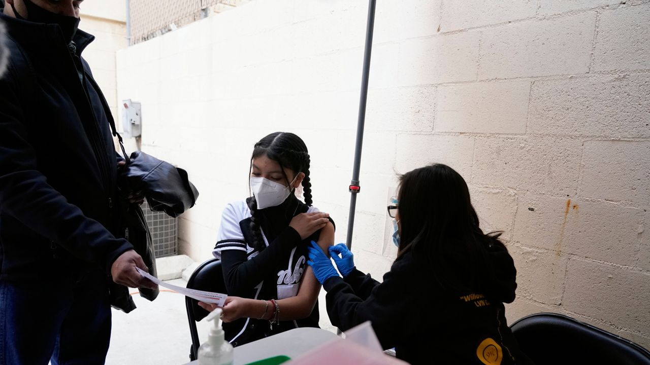 Leslie Flores, center, of Tijuana, Mexico, looks over documents with her father, Jack Flores, left, before receiving a vaccination shot against the coronavirus outside of the Mexican Consulate building, Thursday, Nov. 18, 2021, in San Diego. (AP Photo/Gregory Bull)