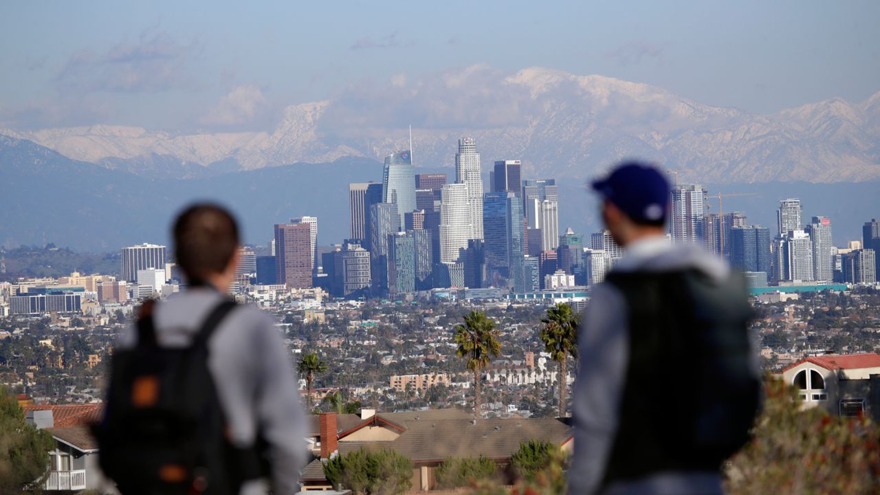 Visitors take in a view as snow covers the San Gabriel Mountains behind the downtown skyline after a series of storms Friday, Dec. 27, 2019, in Los Angeles. (AP Photo/Marcio Jose Sanchez)