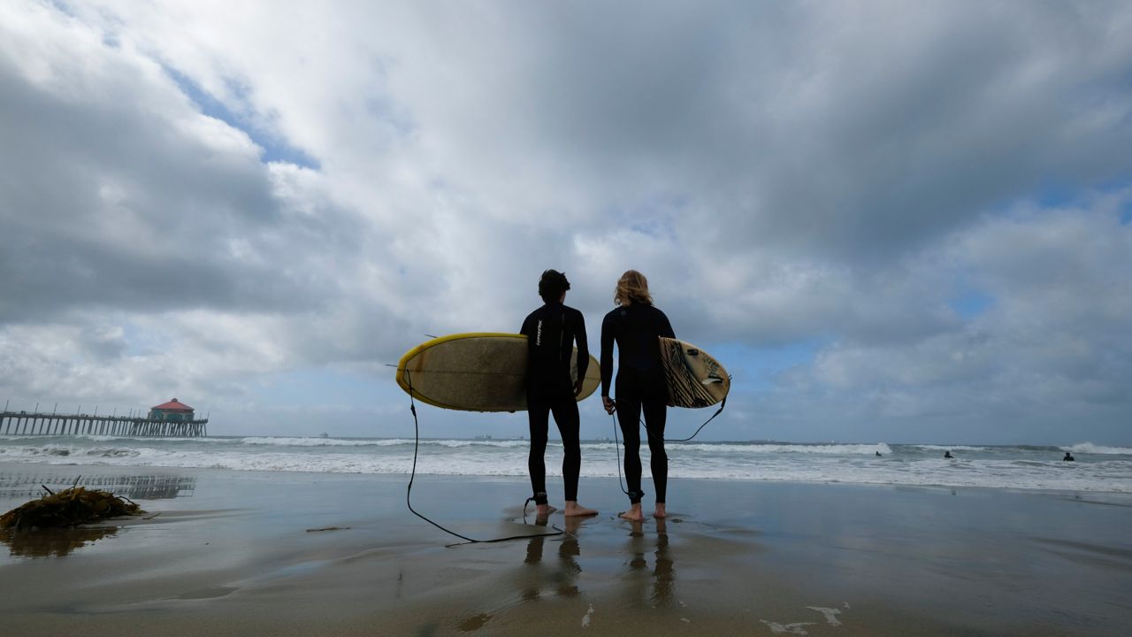 People get ready to surf on a beach in Huntington Beach, Calif., Monday, Oct. 11, 2021. (AP Photo/Ringo H.W. Chiu)