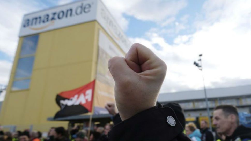 A participant of a demonstration raises his fist in front of the local site of the online retail company Amazon in Leipzig, Germany. (Photo Courtesy: The Associated Press)