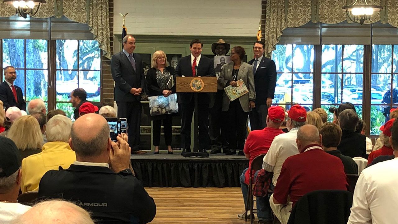 Gov. DeSantis stands on stage with State Sen. Joe Gruters and parents of people killed by undocumented immigrants in The Villages on Monday. (Jesse Canales, Spectrum News)