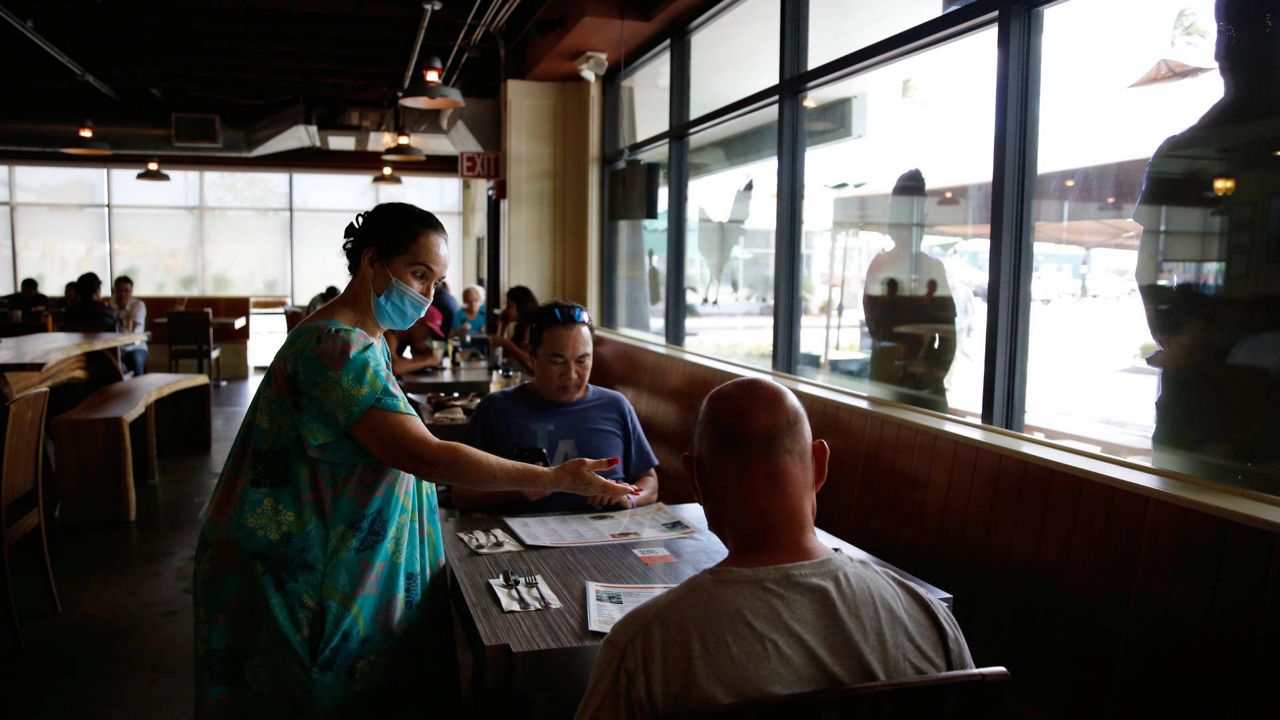 Highway Inn restaurant hostess Kuuipo Lorenzo, left, seats two customers Oct. 25, 2021, in Honolulu. (AP Photo/Caleb Jones)
