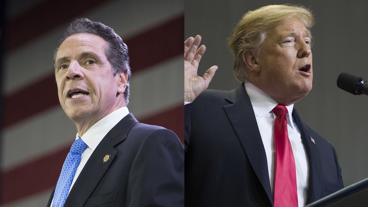 From left to right: New York Gov. Andrew Cuomo wearing a black suit jacket, a white dress shirt, and a blue tie while standing in front of an American flag; President Donald Trump wearing a black suit jacket, a white dress shirt, and a red tie speaking into a black microphone.