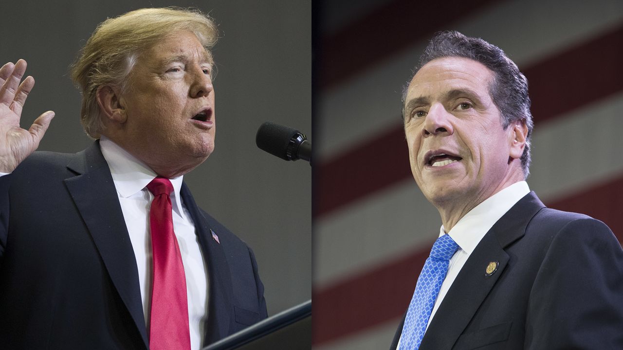 From left to right: President Donald Trump wearing a black suit jacket, a white dress shirt, and a red tie speaking into a black microphone; New York Gov. Andrew Cuomo wearing a black suit jacket, a white dress shirt, and a blue tie while standing in front of an American flag.