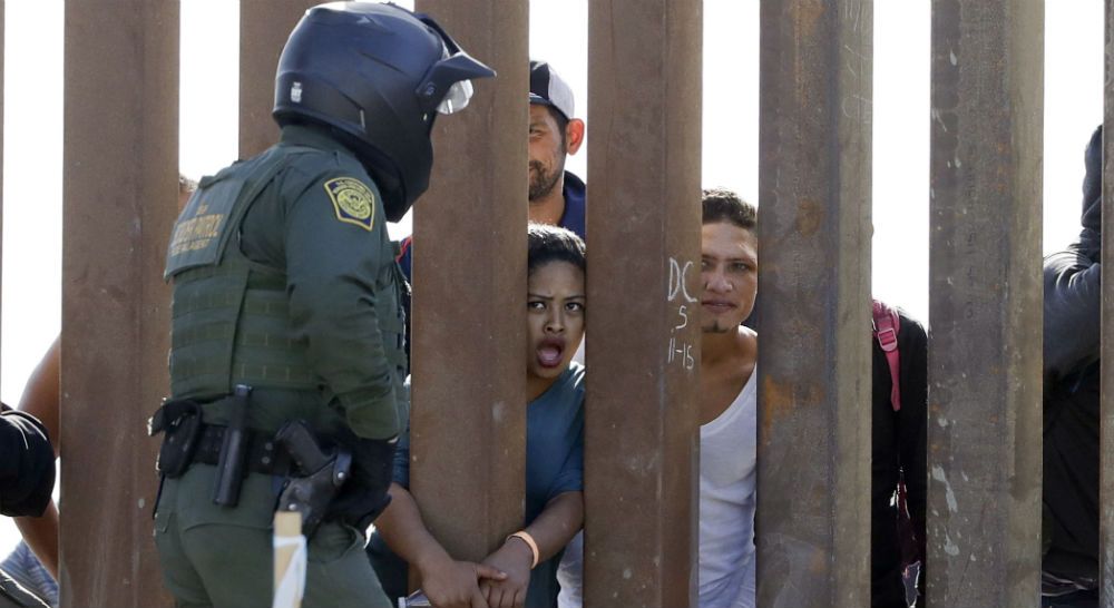 Migrants from Central America yell through a border wall at a U.S. Border Patrol agent after he pulled down a banner Sunday, Nov. 25, 2018, in San Diego. Migrants approaching the U.S. border from Mexico were enveloped with tear gas Sunday after a few tried to breach the fence separating the two countries. (AP Photo/Gregory Bull)