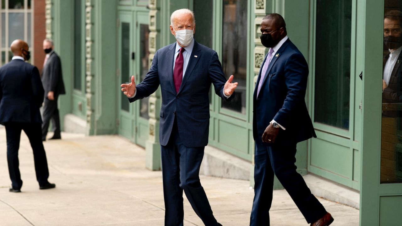 Joe Biden stands on a sidewalk wearing a face mask