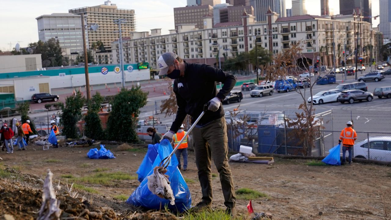 California Gov. Gavin Newsom and CalTRans crews pick up litter along the CA-101 freeway overlooking Los Angeles Wednesday, Dec. 15, 2021. (AP Photo/Damian Dovarganes)