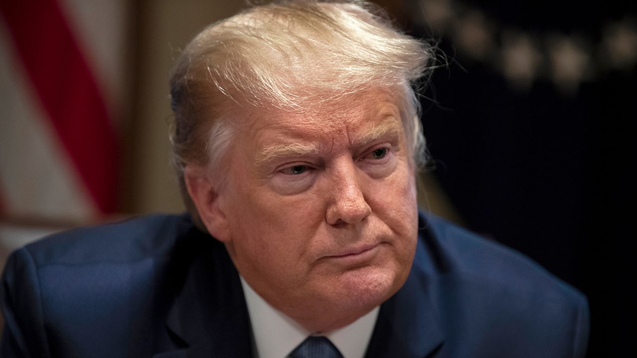 President Donald Trump, wearing a navy blue suit jacket, a white dress shirt, and a tie.