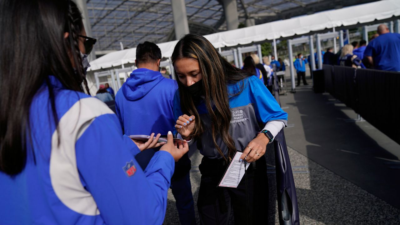 A worker checks proof of vaccination as fans enter SoFi Stadium amid the COVID-19 pandemic before an NFL football game between the Los Angeles Rams and the Jacksonville Jaguars Sunday, Dec. 5, 2021, in Inglewood, Calif. (AP Photo/Jae C. Hong)