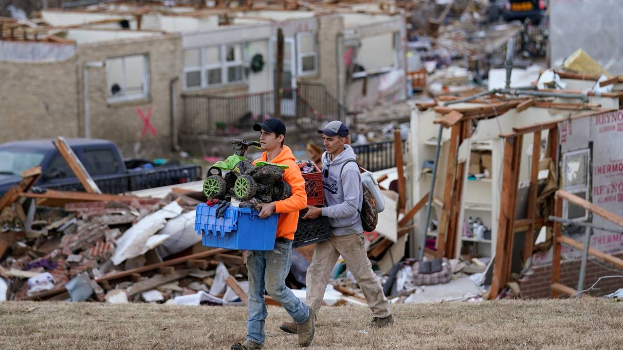 Travis Lussier, left, and Joshua Lee carry possessions from Joshua's destroyed apartment in the aftermath of tornadoes that tore through the region, in Dawson Springs, Ky., Wednesday, Dec. 15, 2021. Americans across the country are pitching in to help after last week’s tornadoes ravaged the South and Midwest, killing at least 90 people and displacing hundreds. (AP Photo/Gerald Herbert, File)