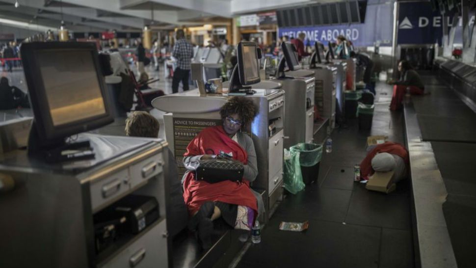 Passengers rest behind the ticket counter after the lights went out at Hartfield-Jackson Atlanta International Airport, Sunday, Dec. 17, 2017, in Atlanta. A sudden power outage at the airport on Sunday grounded scores of flights and passengers during one of the busiest travel times of the year. (AP Photo/Branden Camp)