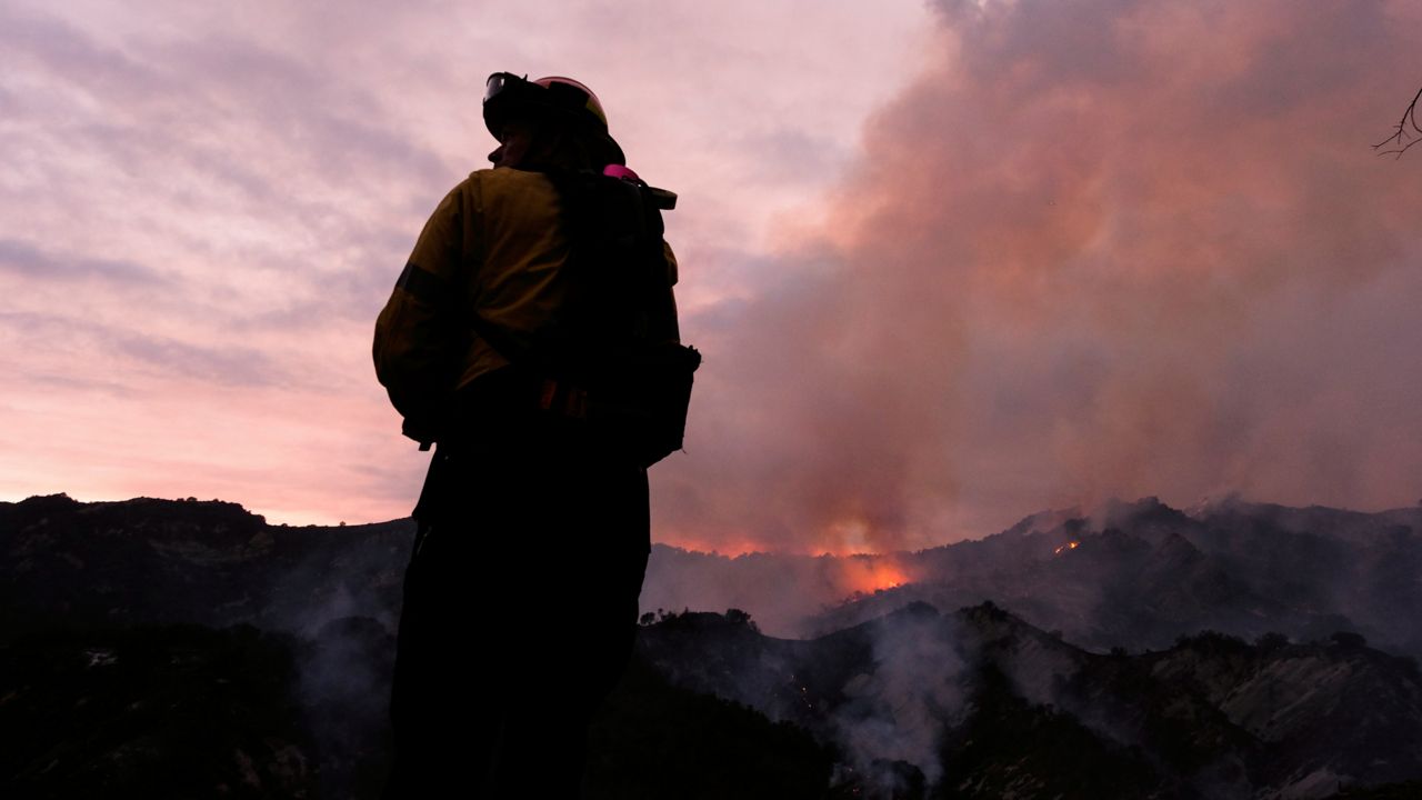 A firefighter watches as smoke rises from a brush fire scorching at least 100 acres in the Pacific Palisades area of Los Angeles Saturday, May 15, 2021. (AP Photo/Ringo H.W. Chiu)