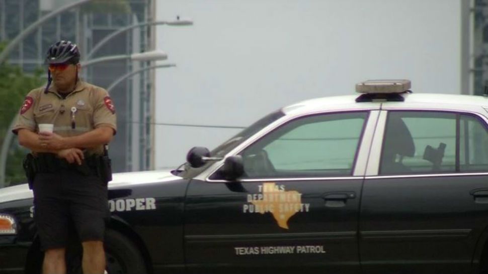A Texas Trooper leans against a patrol vehicle. 