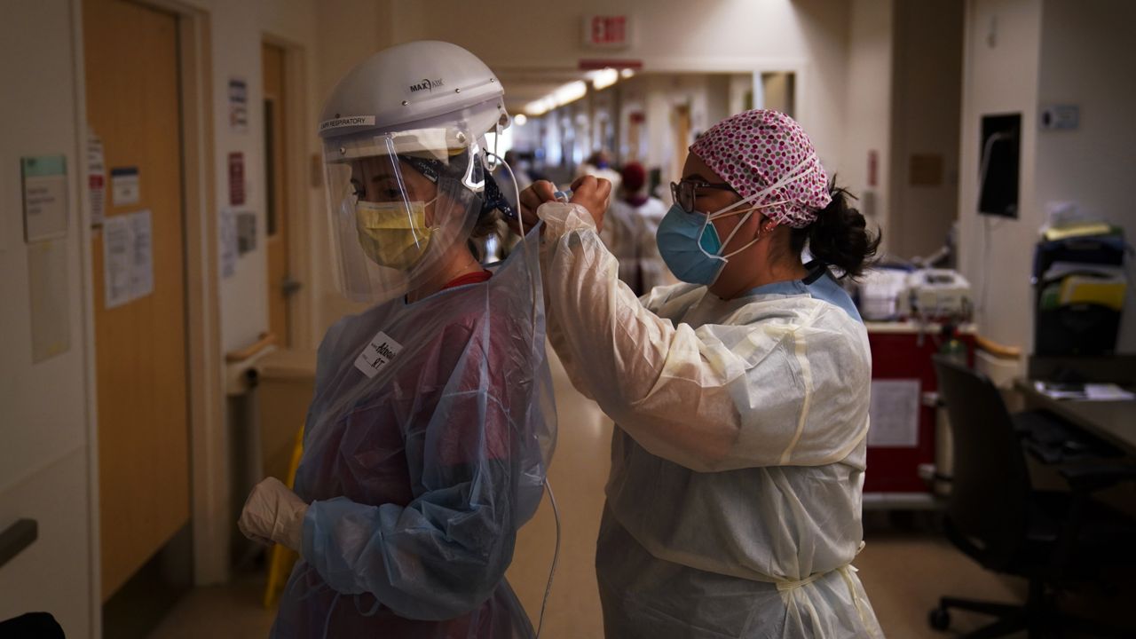 Registered nurse Dania Lima, right, helps fellow nurse Adriana Volynsky put on her personal protective equipment in a COVID-19 unit at Providence Holy Cross Medical Center in Mission Hills on Dec. 22, 2020. (AP/Jae C. Hong)