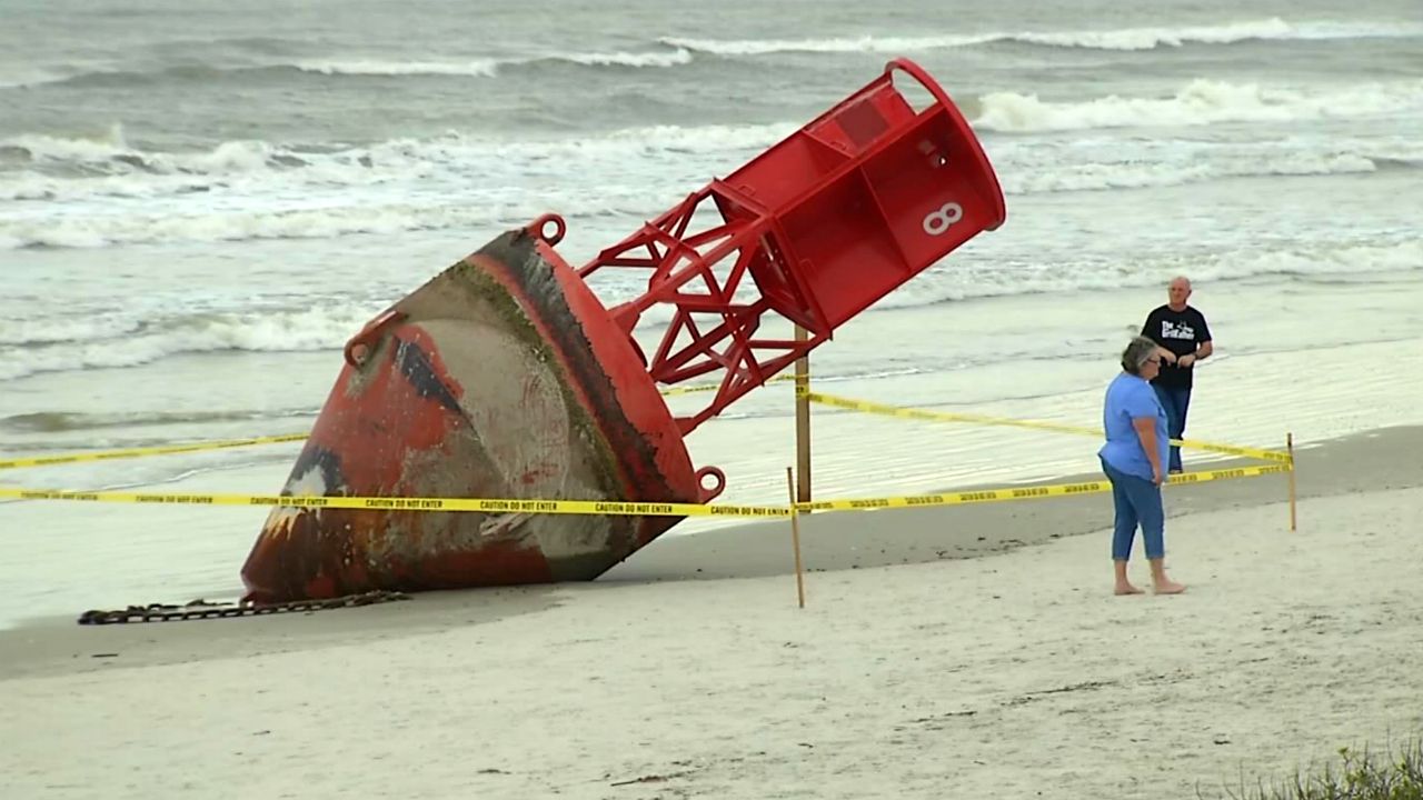 A 13,000-pound Coast Guard buoy that beached at New Smyrna Beach attracted crowds Monday. The Coast Guard says it likely is from the Charleston, South Carolina area. (Arnie Girard/Spectrum News)