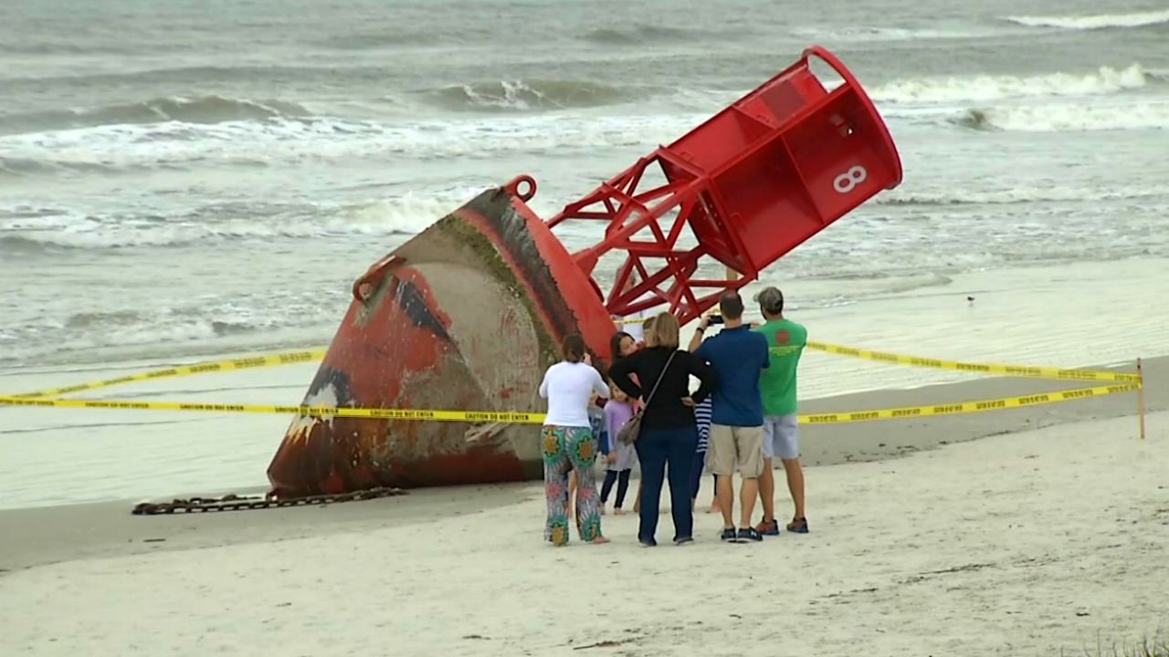 A 13,000-pound Coast Guard buoy that beached at New Smyrna Beach attracted crowds Monday. The Coast Guard says it likely is from the Charleston, South Carolina area. (Arnie Girard/Spectrum News)