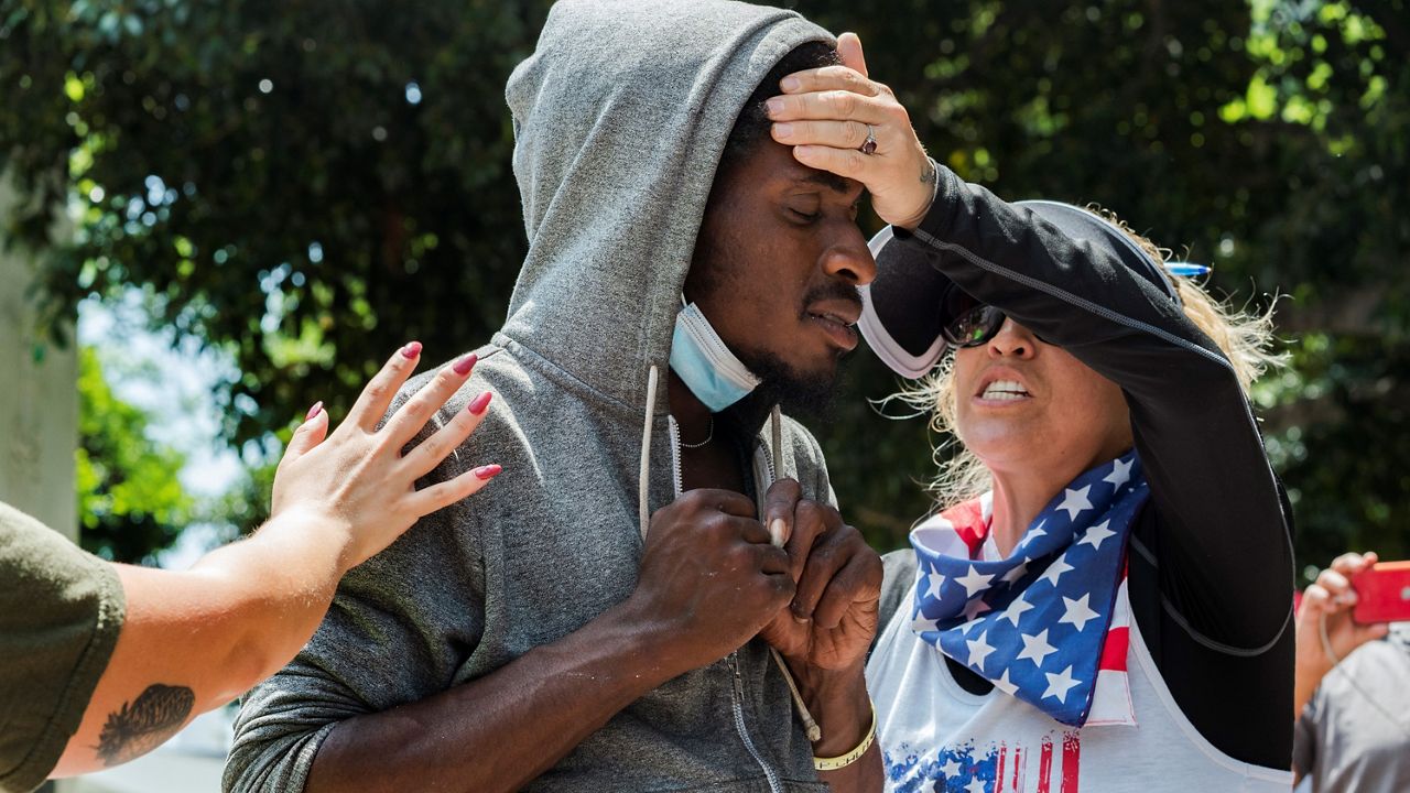 Anti-vaccine demonstrator Stacey Hidalgo, right, comforts an unidentified homeless man in a moment of prayer during an anti-vaccine rally outside City Hall in Los Angeles on Aug. 14, 2021. (AP Photo/Damian Dovarganes)