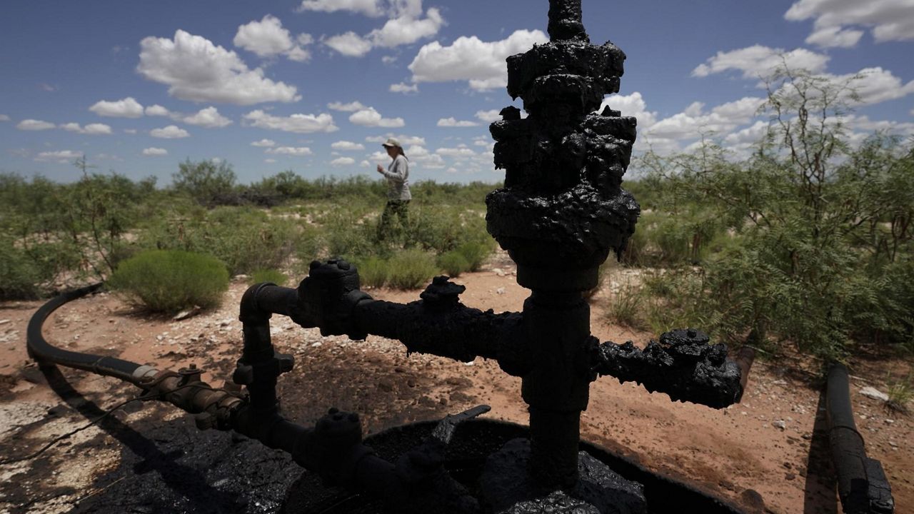 Ashley Williams Watt walks near a wellhead and flowline at her ranch, Friday, July 9, 2021, near Crane, Texas. The wells on Watt's property seem to be unplugging themselves. Some are leaking dangerous chemicals into the ground, which are seeping into her cattle's drinking water. And she doesn't know how long it's been going on. (AP Photo/Eric Gay)