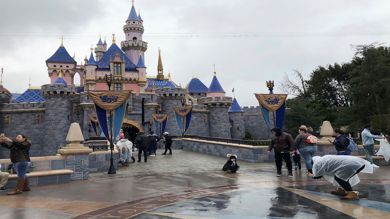 In this March 13, 2020, file photo, visitors take photos at Disneyland in Anaheim, Calif. Disney is proposing to reopen its Southern California theme parks in mid-July after a four-month closure due to the coronavirus, the company said on Wednesday. Disney Parks, Experiences and Products said in a statement that the goal is to reopen Disneyland and Disney California Adventure on July 17. A nearby Disney-themed shopping area would reopen on July 9. (AP Photo/Amy Taxin, File)