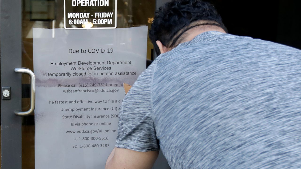 In this file photo, a man takes a photo of a sign advising that the Employment Development Department is closed due to coronavirus concerns, in San Francisco on March 26, 2020. (AP Photo/Jeff Chiu)
