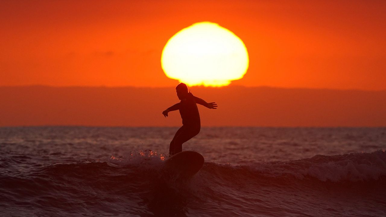 In this file photo, a surfer rides a wave as the sun goes down the day before the beach is scheduled to close during the coronavirus outbreak on April 30, 2020, in Newport Beach. (AP Photo/Mark J. Terrill)