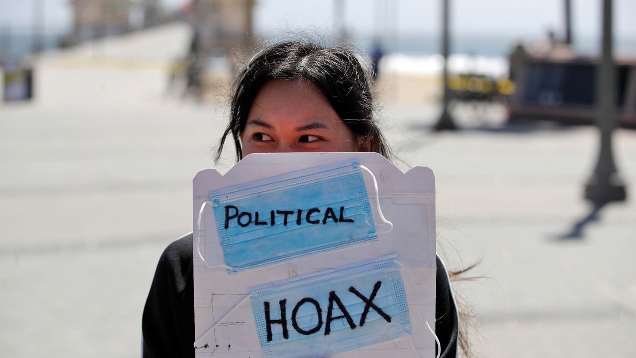 In this file photo from May 3, 2020, a protester holds a sign in front of the pier in Huntington Beach. Orange County beaches were singled out for closure by Gov. Gavin Newsom during the coronavirus pandemic. (AP Photo/Marcio Jose Sanchez)