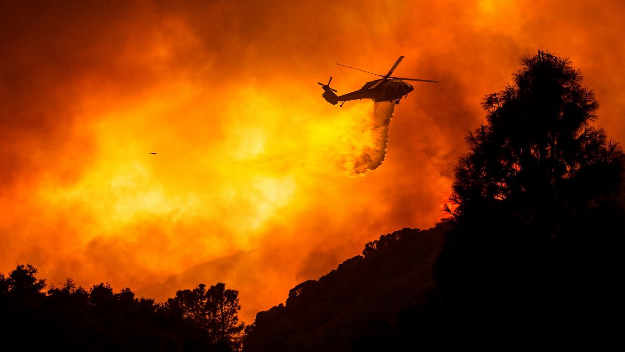 In this file photo from Aug. 12, 2020, a helicopter drops water on the Lake Hughes fire in Angeles National Forest north of Santa Clarita. The fire was 70 percent contained as of Thursday morning. (AP Photo/Ringo H.W. Chiu)