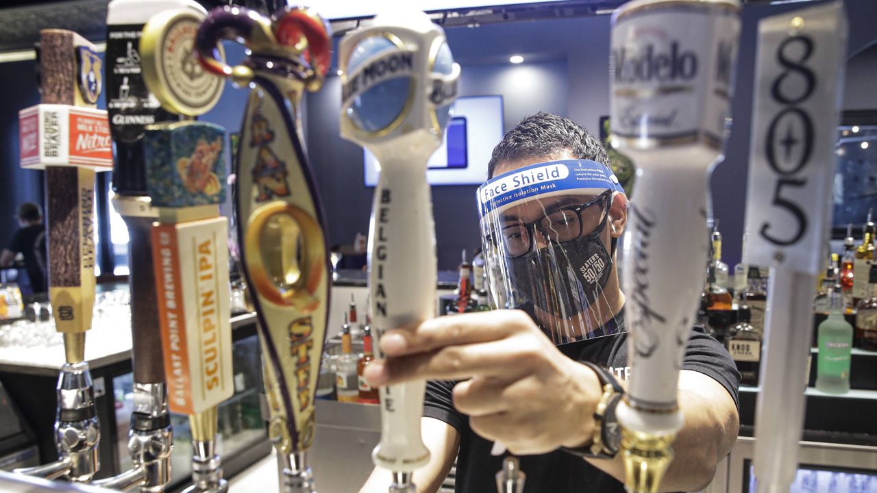 A bartender pours a beer while wearing a mask and face shield amid the coronavirus pandemic at Slater's 50/50 Wednesday, July 1, 2020, in Santa Clarita, Calif. (AP Photo/Marcio Jose Sanchez)