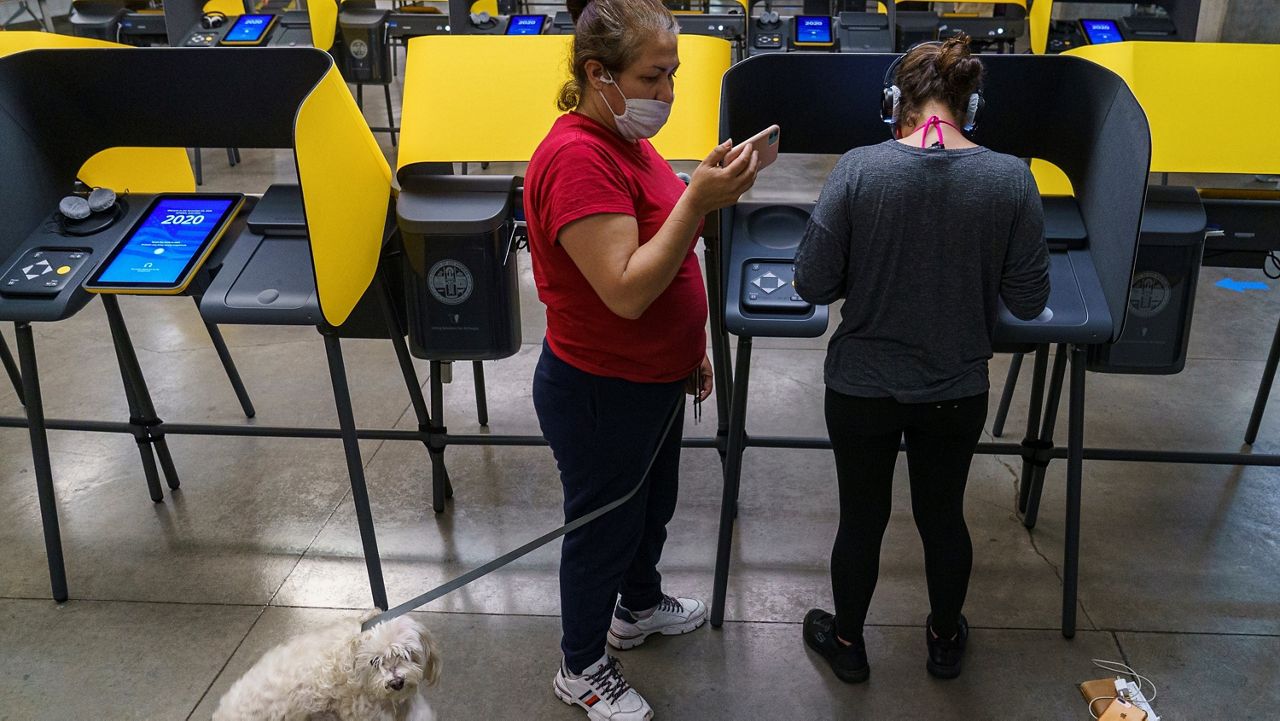 First-time voter Berlyn Gonzalez votes as her mother, Claudia Gonzalez, holds the leash to her dog Nenengue, in Los Angeles on Tuesday, Nov. 3, 2020. (AP Photo/Damian Dovarganes)
