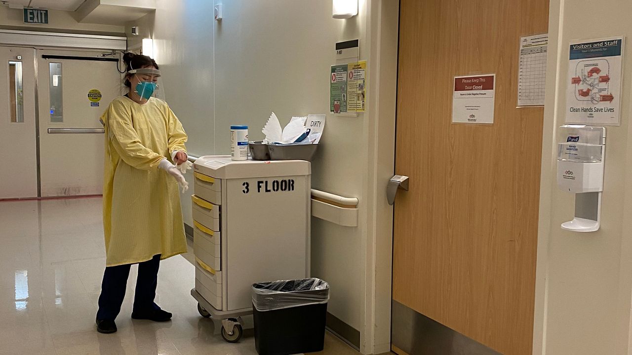 A physician puts on gloves while standing outside a hospital room.