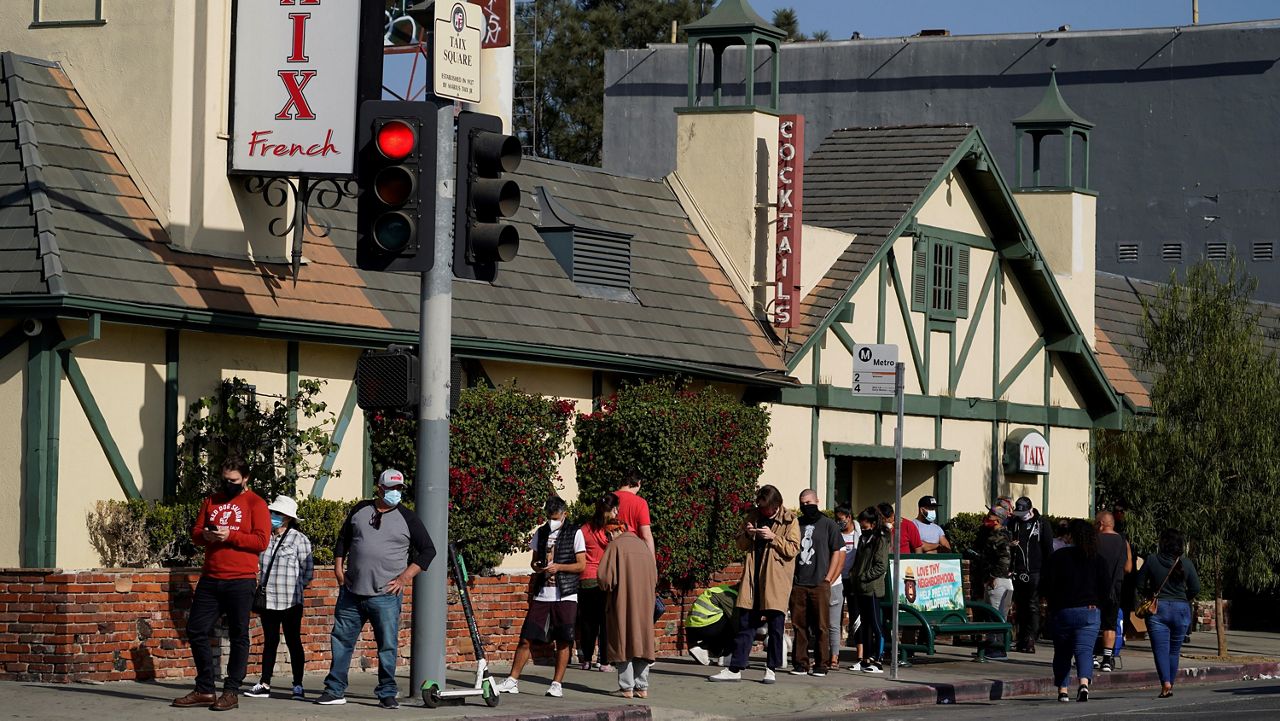 In this file photo from Dec. 10, 2020, people wait in line on Sunset Boulevard, next to a restaurant, for a free COVID-19 test at a library branch in Los Angeles. (AP Photo/Damian Dovarganes)