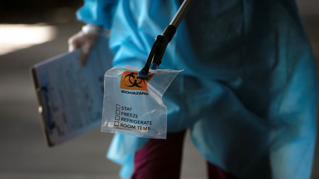 In this file photo from July 16, 2020, a physician assistant carries a nasal swab sample using a grabber at a COVID-19 drive-through testing site set up at the Anaheim Convention Center in Anaheim. (AP Photo/Jae C. Hong)