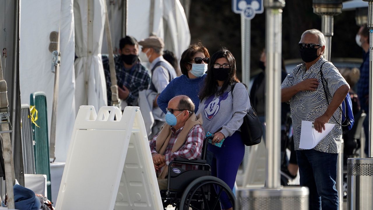 Orange County residents wait in line outside tents for a COVID-19 vaccine at the Toy Story parking lot at the Disneyland Resort Wednesday, Jan. 13, 2021, in Anaheim, Calif. (AP Photo/Damian Dovarganes)