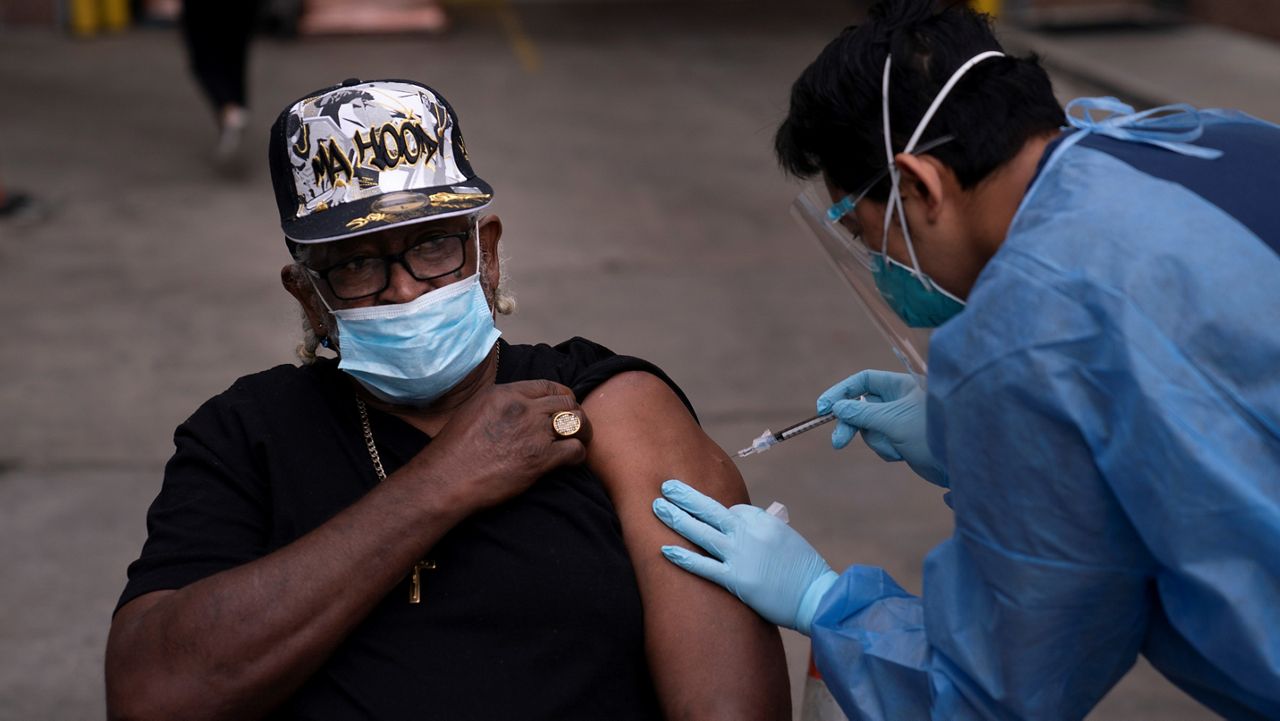 In this file photo from Feb. 10, 2021, registered nurse Angelo Bautista, right, administers a COVID-19 vaccine to Tyrone Valiant, 73, at a vaccination site set up in the parking lot of the Los Angeles Mission in the Skid Row area of Los Angeles. (AP Photo/Jae C. Hong)